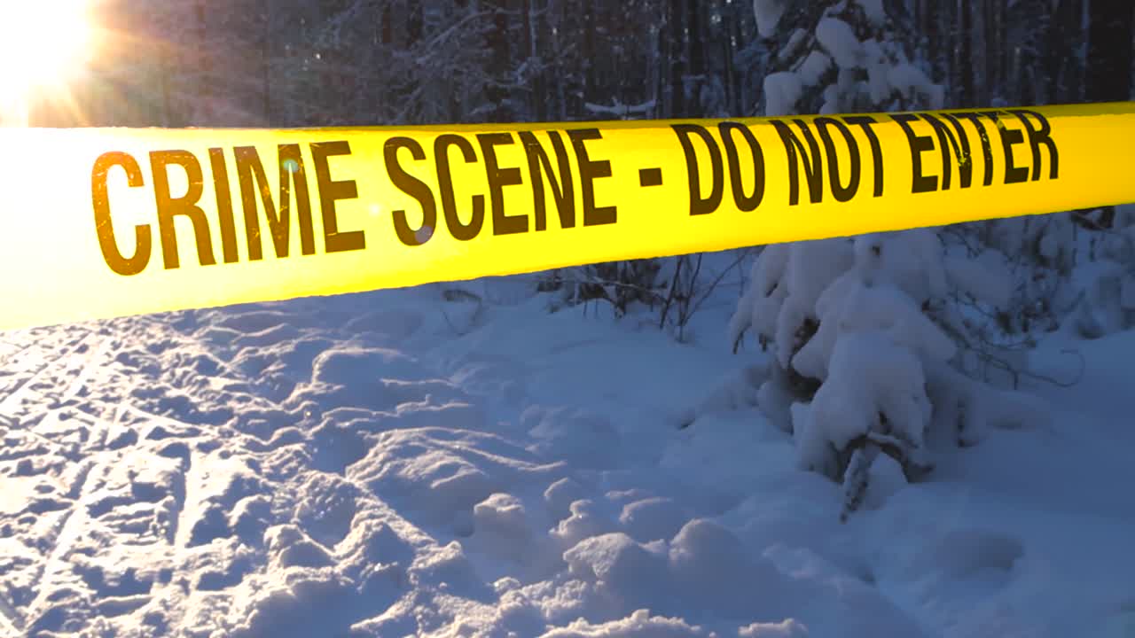 Backlit police barrier ribbon over snowy path with footprints in cold woodland setting