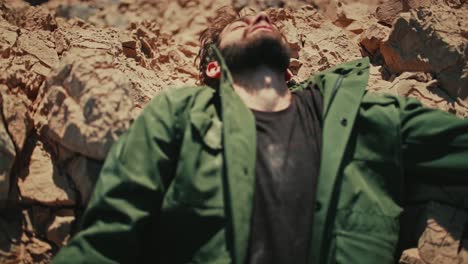 man with beard falls backwards painfully onto rugged desert rocks, top view