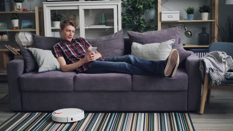 man relaxing on sofa while robot vacuum cleans the floor