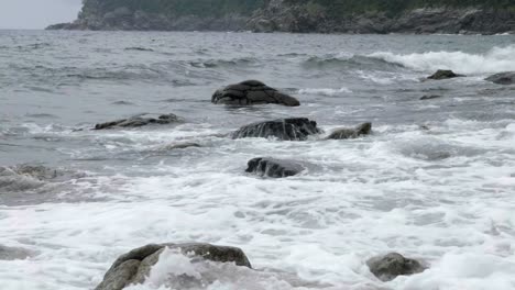 view across coastal waters as waves crash over rocks poking through flowing ocean movement