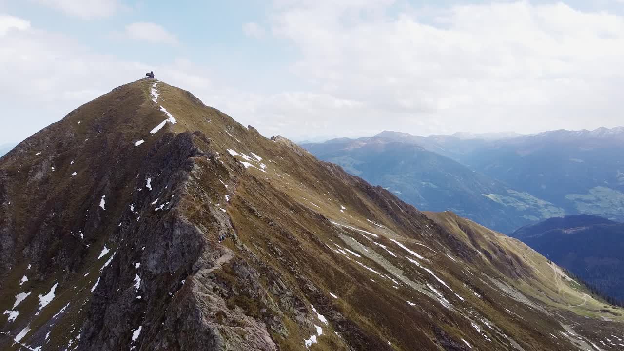 antena cinematográfica de la cima de la montaña de los alpes con una vieja capilla de madera en un pico empinado
