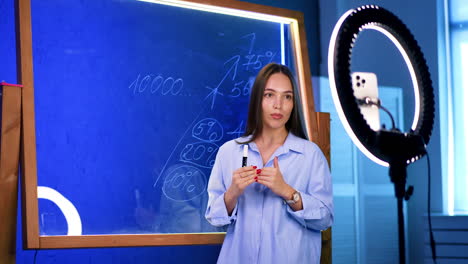 teacher in modern classroom. a young woman teaches at a chalkboard, lit by a ring light, creating a vibrant educational vibe