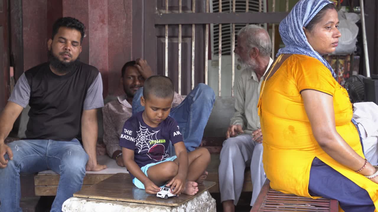 Little Indian boy playing with car toy sitting on a streetside corner with family members