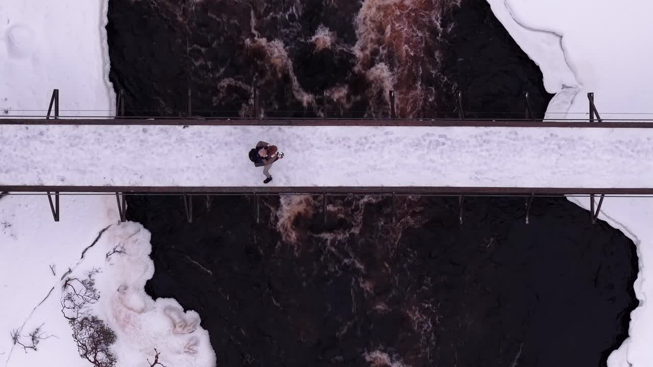 Coppia di influencer sui social media che posano e si abbracciano su un ponte innevato sopra il fiume, vista aerea