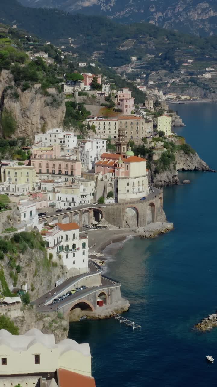 Malebný vertikální letecký pohled z dronu na klikatou silnici Amalfitánského pobřeží na útesu, procházející historickými městy Amalfi a Atrani podél Středozemního moře.