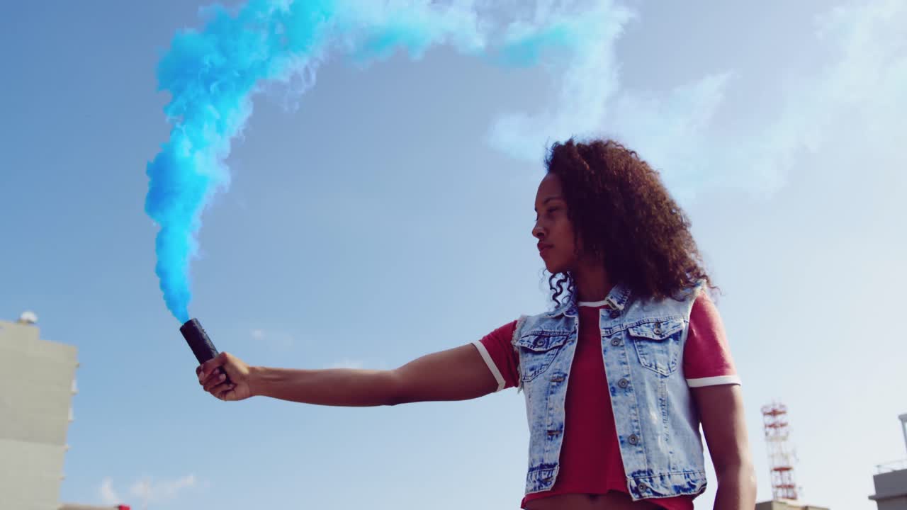 Fashionable young woman on urban rooftop using a smoke grenade