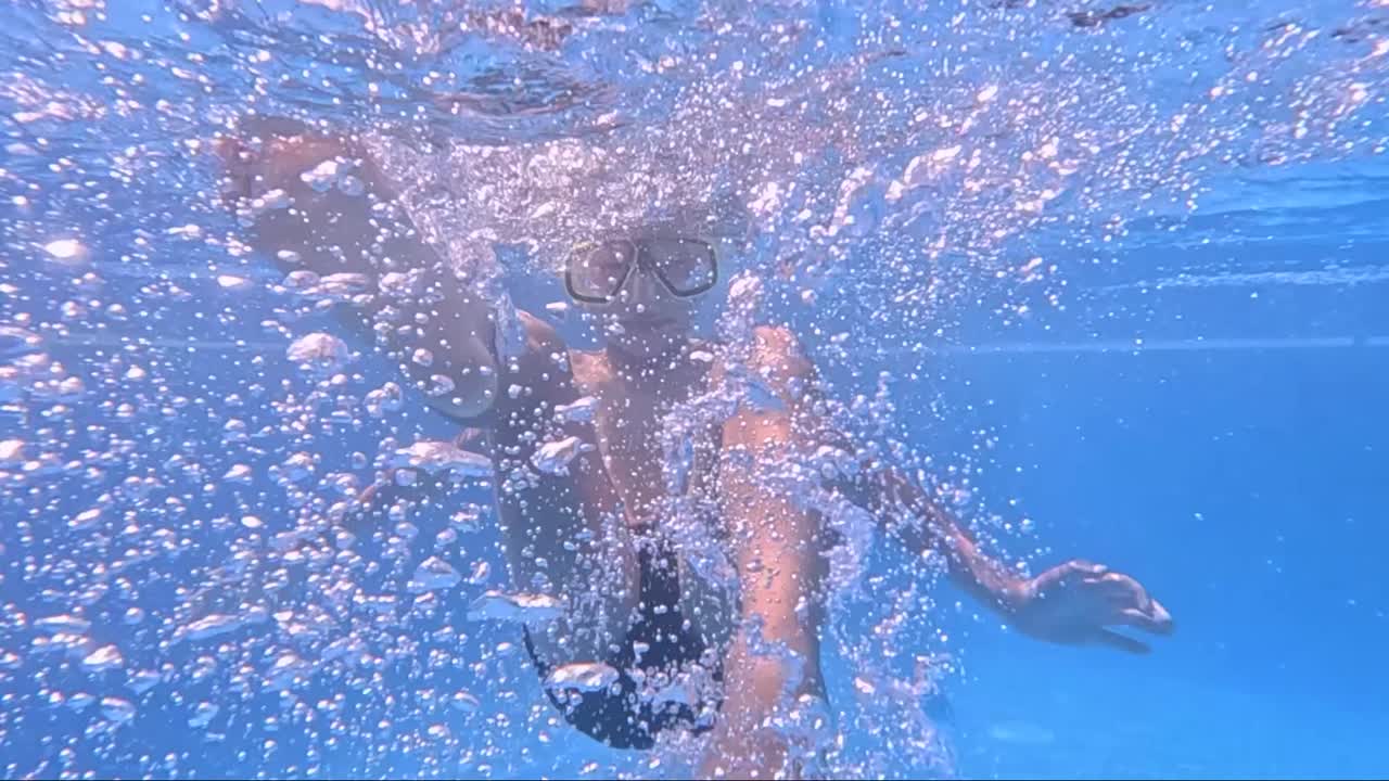 A young swimmer dives beneath the surface, wearing a mask and fins, surrounded by shimmering bubbles and vibrant light. Joy and curiosity radiate as he enjoys the water