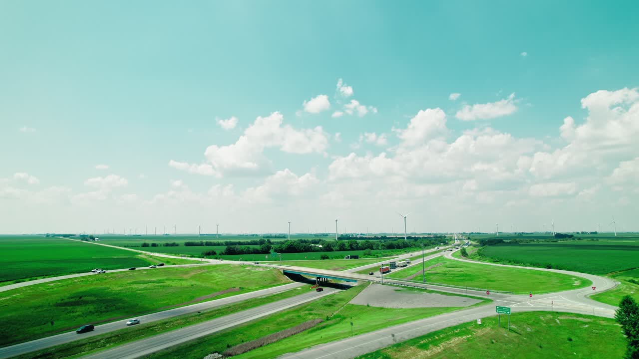 Semi trucks on Intestate I-65 in Indiana, USA with wind farm turbines in background. Logistics Infrastructure and renewable energy. Drone view of the elevated road, traffic junctions and green garden