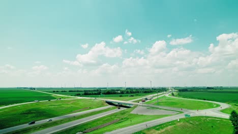 semi trucks on intestate i-65 in indiana, usa with wind farm turbines in background. logistics infrastructure and renewable energy. drone view of the elevated road, traffic junctions and green garden