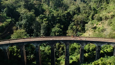 Aerial-of-famous-nine-arch-bridge-in-Ella,-Sri-Lanka-with-blue-train