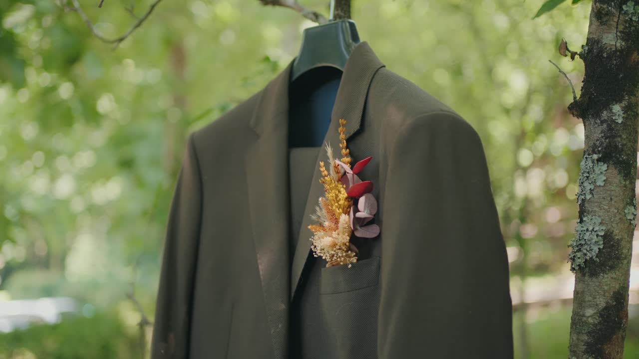 햇빛이 잘 드는 나무에 말린 꽃 부토니에가 걸려 있는 신랑의 갈색 정장