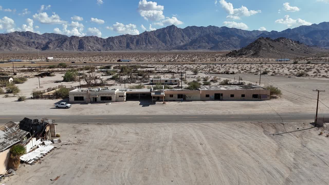 Vista aerea di un edificio abbandonato nel deserto, autostrada di fronte alle montagne, cielo azzurro con poche nuvole, Interstate 10 a Desert Center, California, auto e semirimorchi che percorrono la strada
