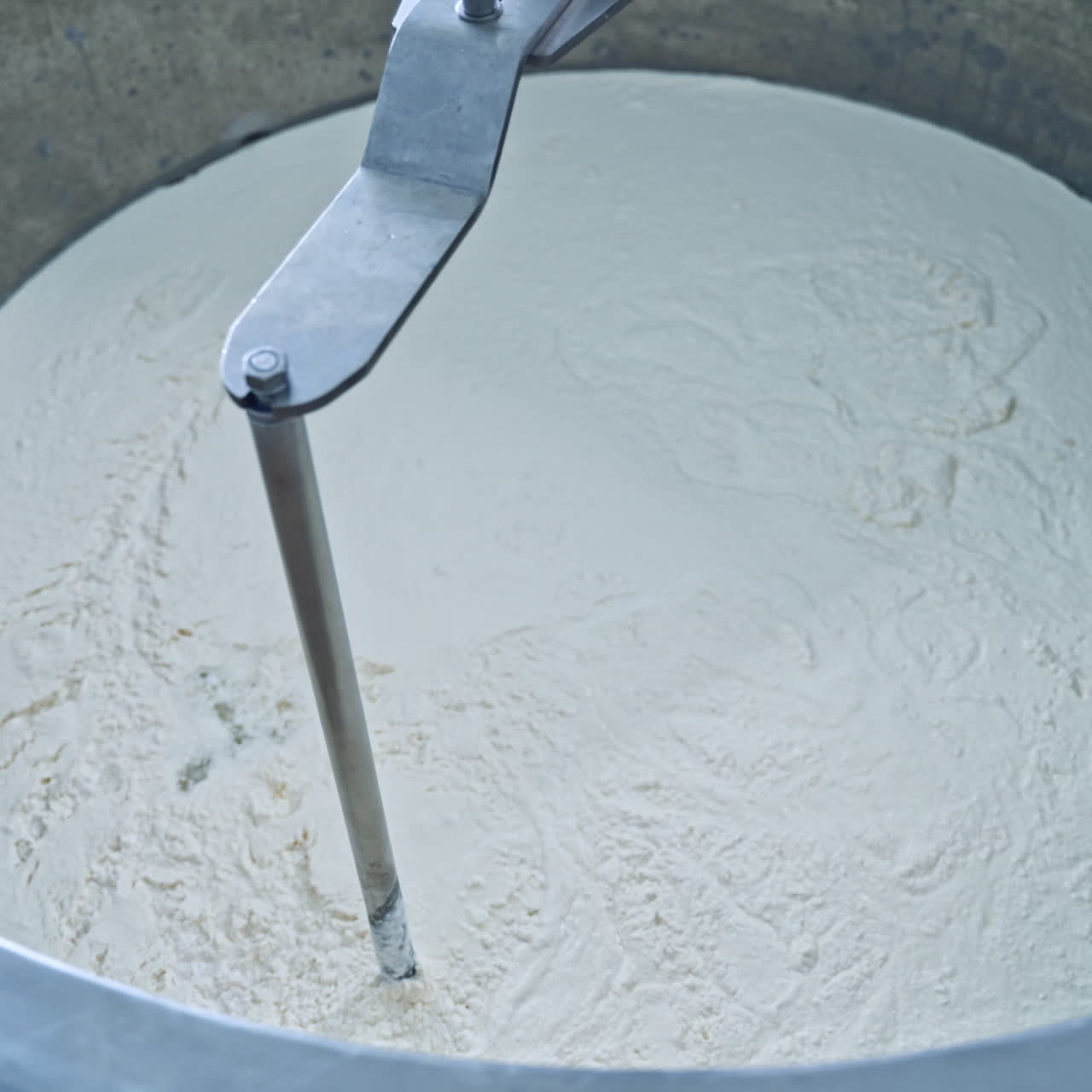 Factory equipment close-up. Metal mixing apparatus boils and mix milk for making cheese at milk products making factory in slow motion.