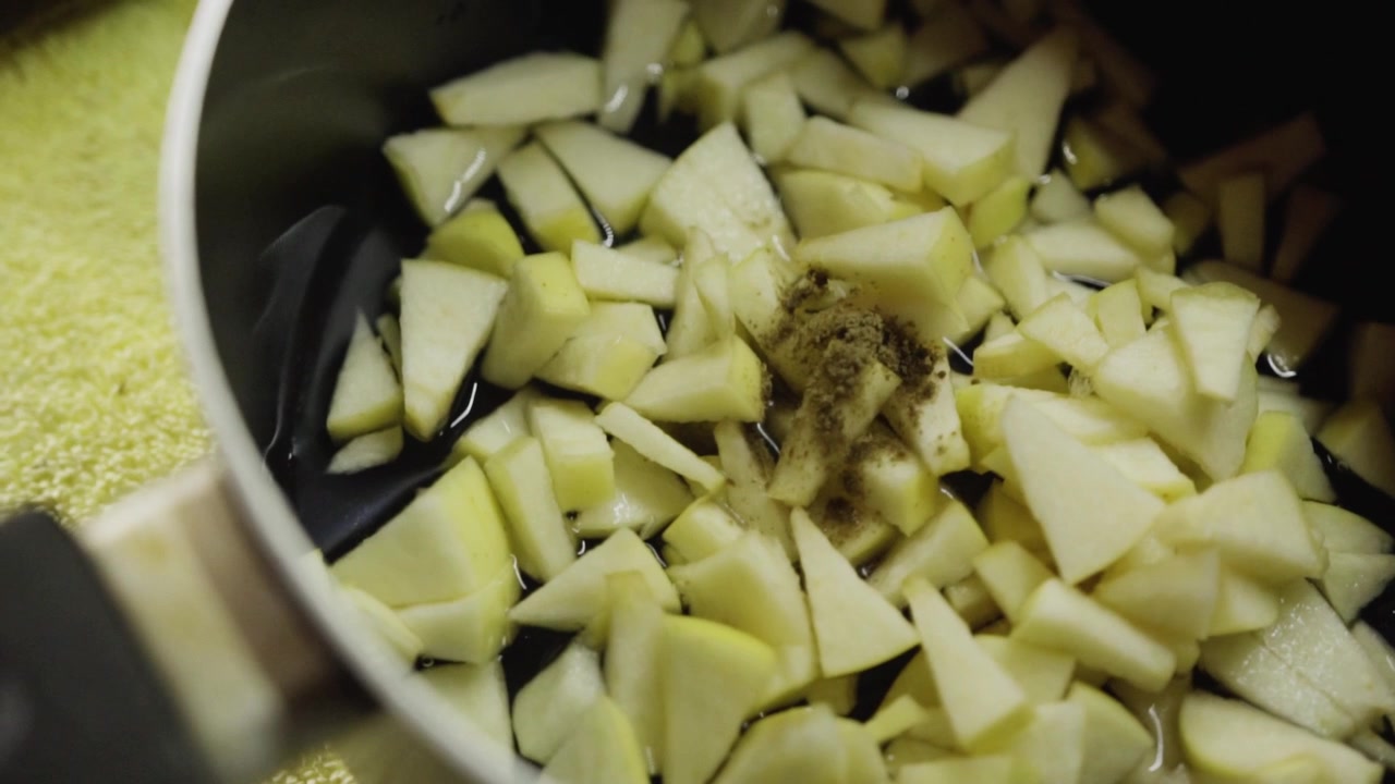 Closeup view of chopped apple pieces being stirred inside cooking pot, simple kitchen scene showing fresh fruit preparation for homemade recipe and cooking process