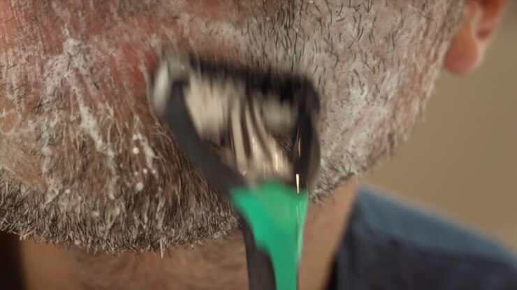 Close up of a man shaving his beard with a green and black razor