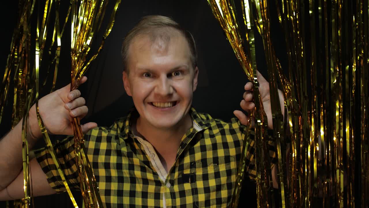 Portræt af kaukasisk mand, der poserer på sort baggrund. Guld skinnende foliestrimler. Fest, musik, disco