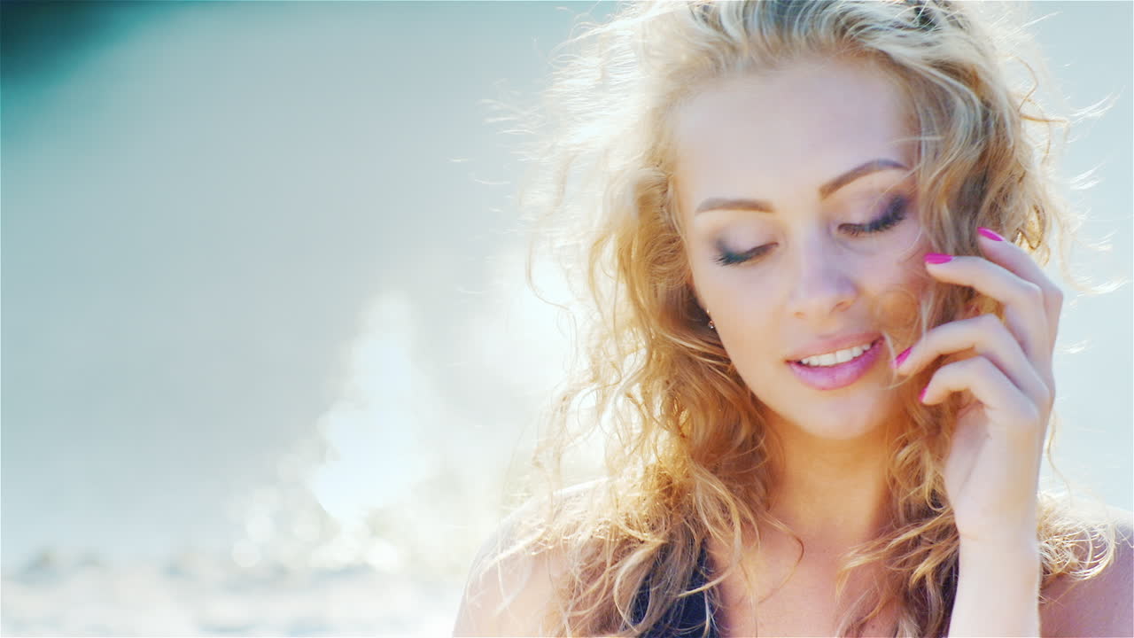 해변 초상화에서 그녀의 아름다운 머리를 가지고 노는 카메라에 미소 짓는 젊은 여자