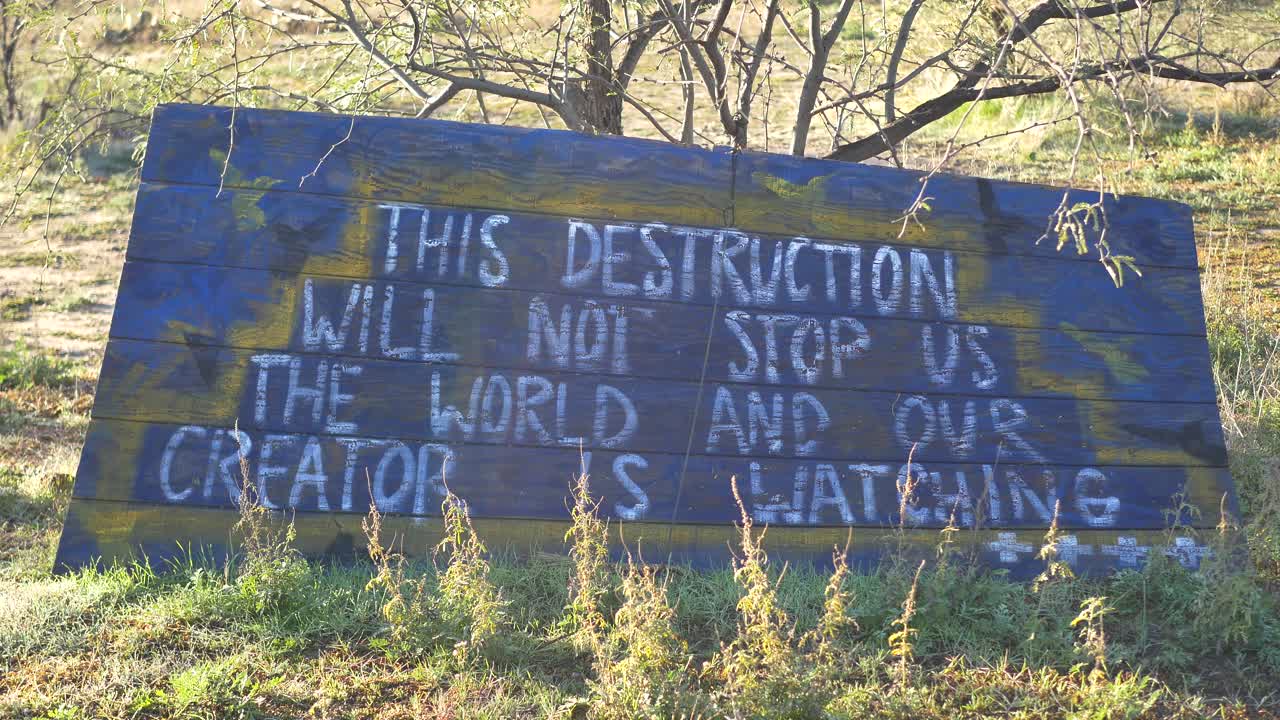 Un cartello a un tributo in una terra sacra Apache in Arizona che recita "Questa distruzione non ci fermerà - Il mondo e il nostro Creatore stanno guardando"