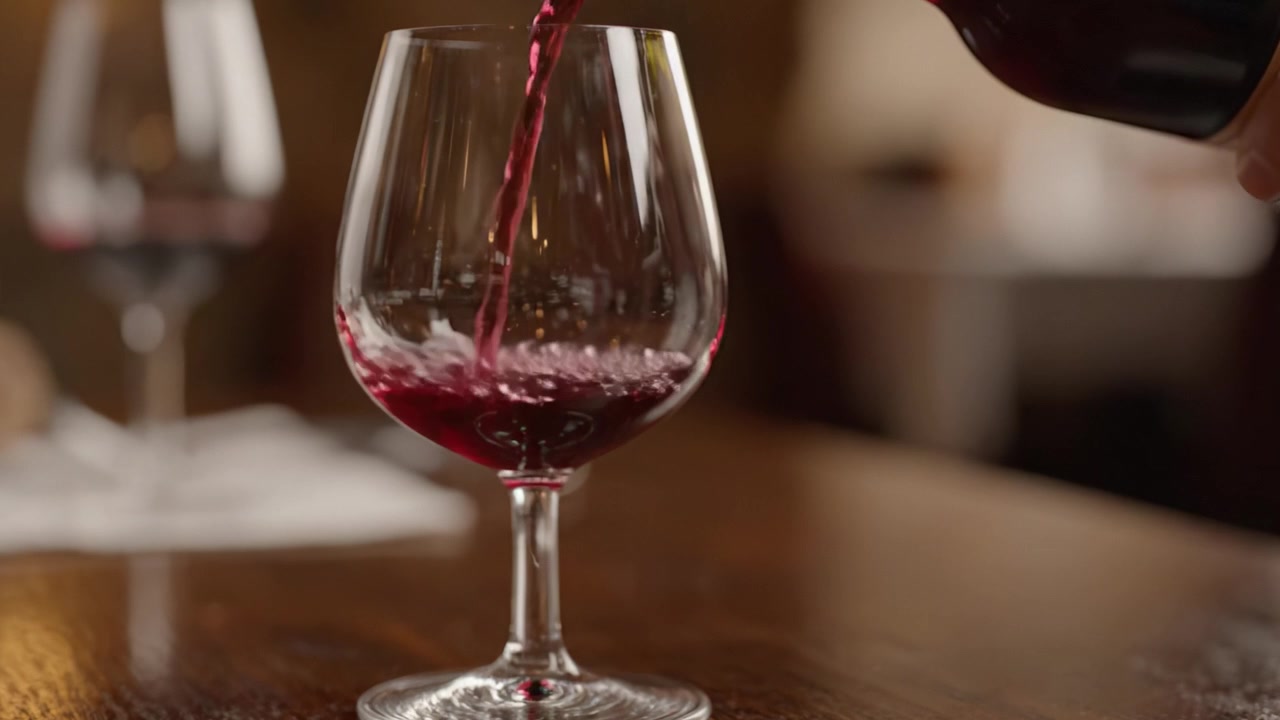 Un sumiller sirviendo vino tinto rico y oscuro en una copa de cristal para realzar el sabor y el aroma, destacando el arte del servicio del vino en una experiencia gastronómica de alta cocina.