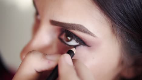 professional makeup artist lining inner eye rim - working in beauty fashion industry cosmetics backstage professional make-up - macro close-up beautiful natural lighting. slow motion. high angle view