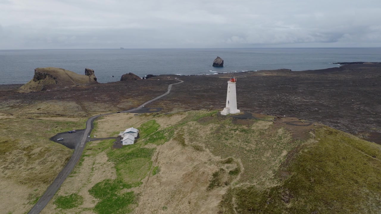 El Faro de Reykjanesviti se alza sobre Baejarfell, sobre terreno volcánico en la península de Reykjanes, Reykjanesbaer, Península del Sur, Islandia, con el Atlántico al fondo durante un deslizamiento de dron