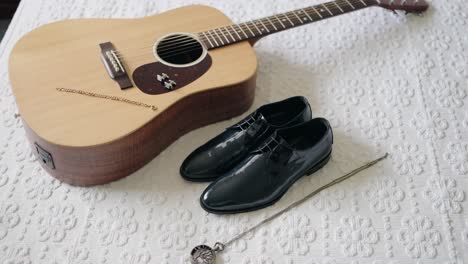 zapatos de vestir negros, reloj de bolsillo de época, y una guitarra acústica cuidadosamente colocada en una superficie blanca con patrones