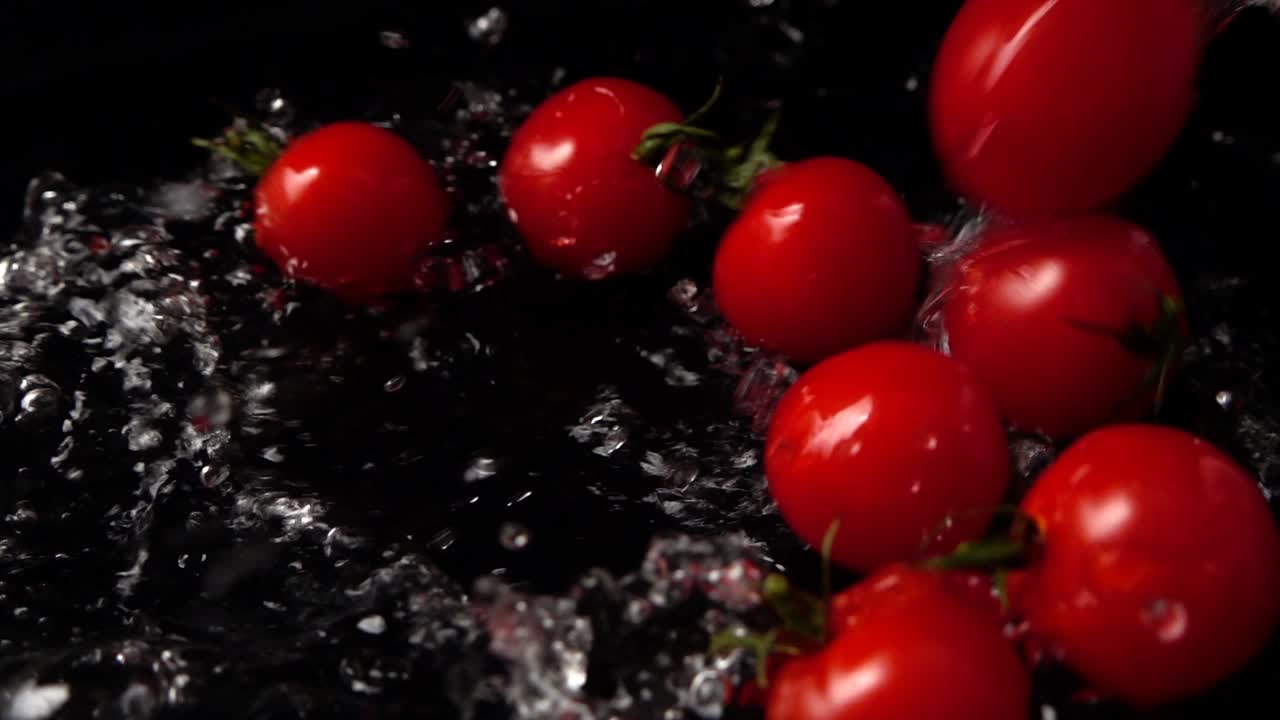 Fallende Kirschtomaten im Wasser auf schwarzem Hintergrund. Zeitlupe.