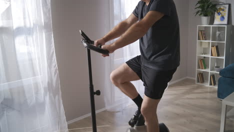 Heimtrainer-Für-Das-Training-Zu-Hause.-Ein-Erwachsener,-Grauhaariger-Mann-Nutzt-Ein-Heimtrainer-Fahrrad-Und-Dreht-Die-Pedale,-Um-Sich-Fit-Zu-Halten.