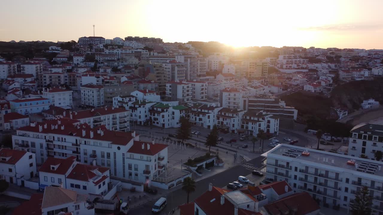 Drone in ascesa sopra il villaggio di Ericeira con un bagliore di sole attraverso i tetti, Portogallo