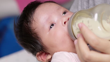 mother feeding her newborn child some infant formula in a feeding bottle that is being held by her mother