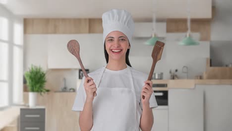 feliz india mujer chef profesional posando con cuchara y espátula