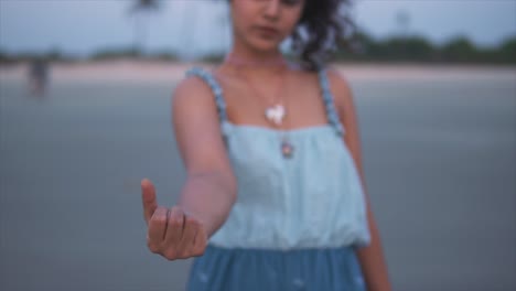 view of young woman holding a shell in hand and gathering a handful, shallow focus, slow motion