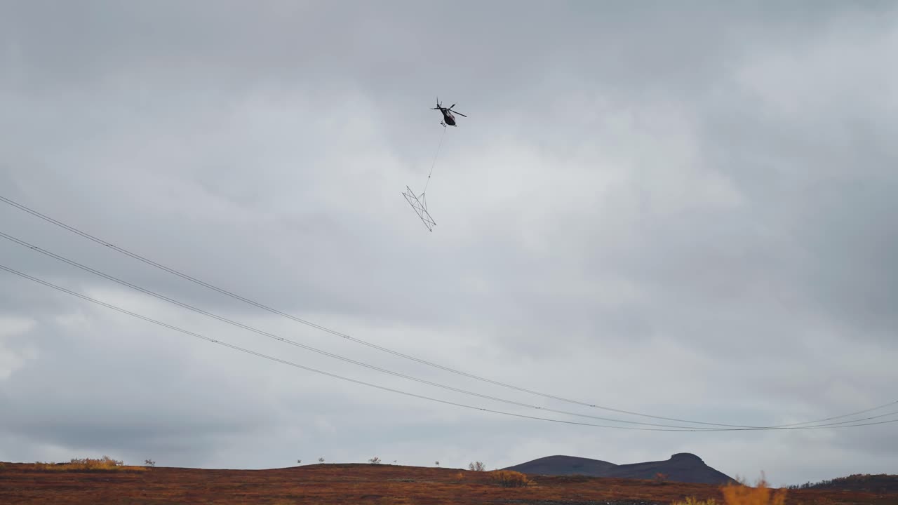 un helicóptero de carga con un cable de elevación y carga conectada hace una entrega en el terreno montañoso de difícil acceso
