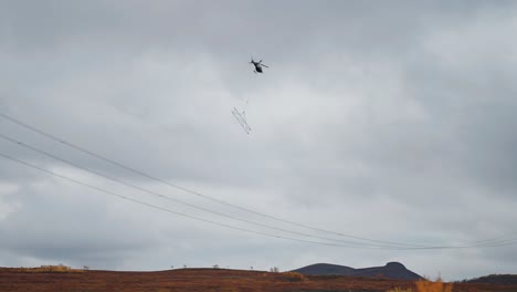 a cargo helicopter with a lifting cable and load attached makes a delivery in the difficult-to-reach mountainous terrain