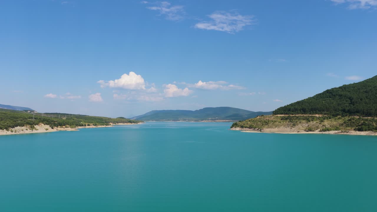 青空の下、緑豊かな山々に囲まれた美しいターコイズ色の湖。