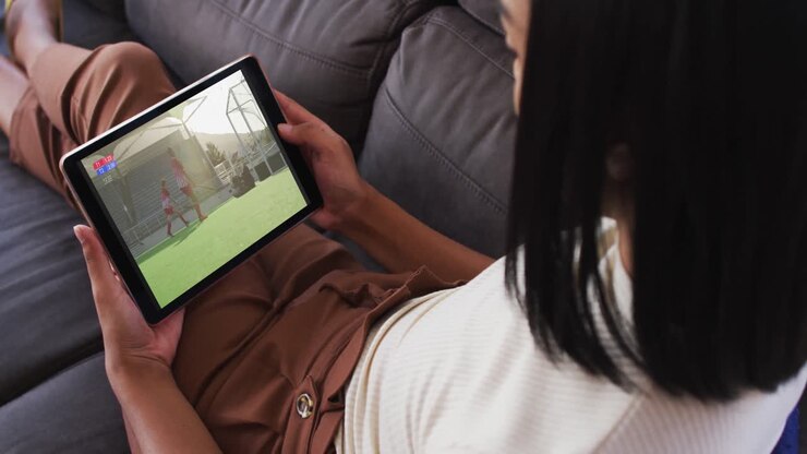 Composito di donna sul divano di casa che guarda una partita di hockey su tablet.