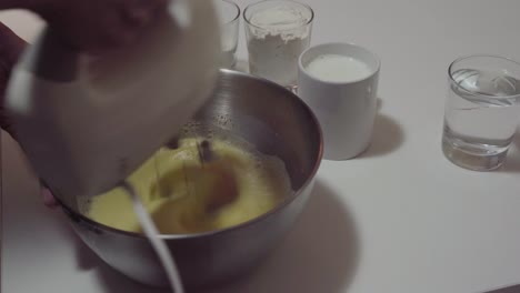 man is beating eggs with the mixer adding ingredients close view