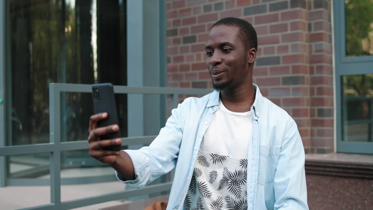 African american student man having a video call on phone in the street near the college