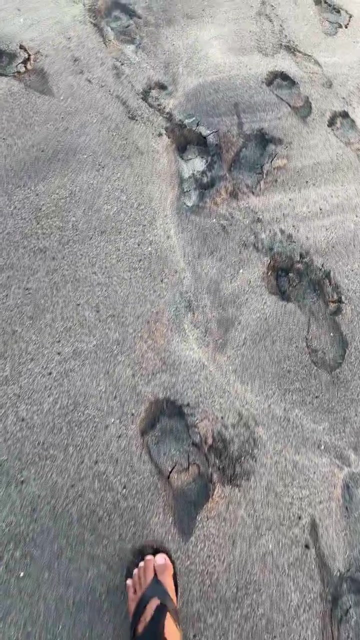 Persona che cammina a piedi nudi su una spiaggia di sabbia vulcanica scura