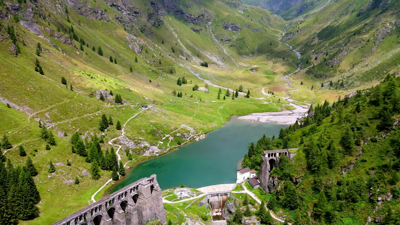 Aerial drone view of Gleno Dam in Val di Scalve, Italian Dolomites and Alpi Orobie. The historic dam is nestled among rugged alpine peaks and lush valleys, creating a dramatic and scenic landscape