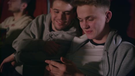 male friends having fun with mobile phone at cinema. gay couple using smartphone