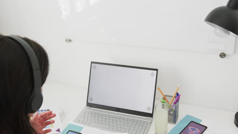 Biracial-female-designer-at-desk-having-video-call-on-laptop-with-copy-space-on-screen,-slow-motion