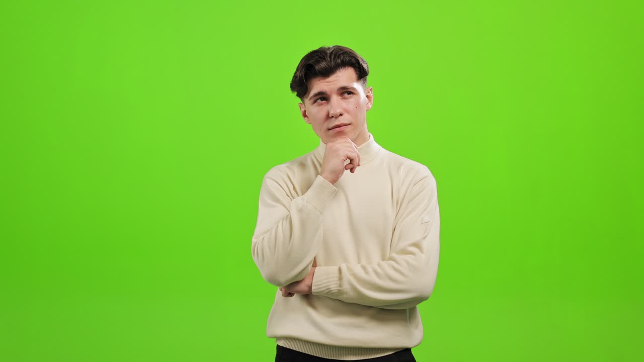 el hombre está de pie y mirando a la cámara. está levantando la mano hasta la barbilla y pensando. está de pie sobre un fondo verde. pantalla verde. 4k.
