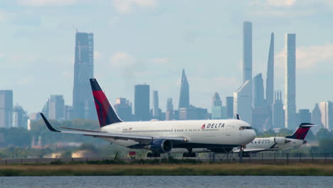 two delta airlines planes taxi on runway at kennedy airport with nyc skyline in background