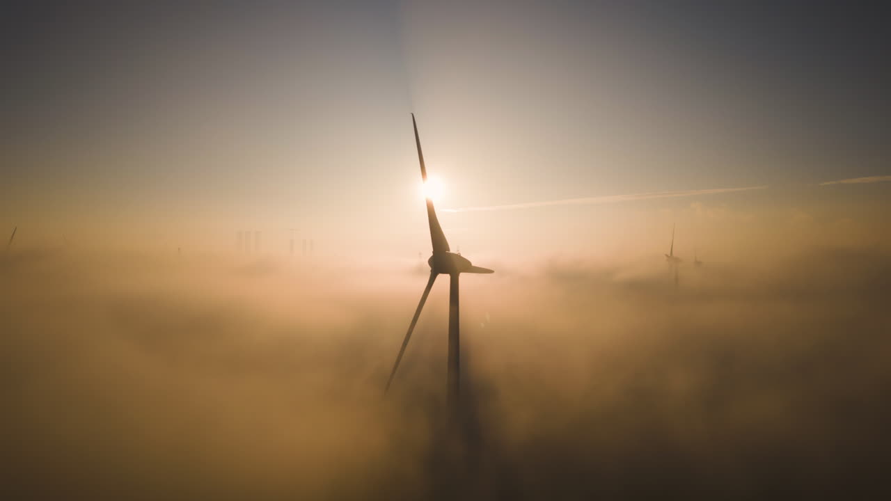 Silhouette of wind turbine casting shadows on clouds and fog below