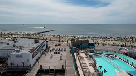 toma aérea de un dron que muestra un concurrido paseo marítimo y una playa llena de gente en un día de verano en la costa de jersey