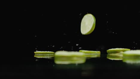 rings of green lime sliced fall on the glass with splashes of water in slow motion.