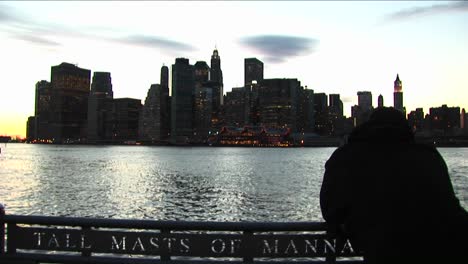 A-Tourist-Leans-Over-Boat-Railing-And-Looks-Across-The-River-Toward-The-South-Street-Seaport-Shore-Of-Manhattan