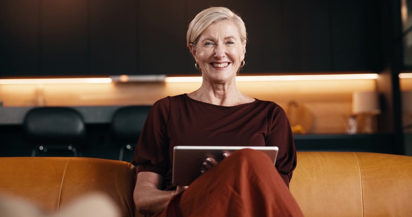 Smiling Mature Woman Using Tablet on Sofa in Modern Home