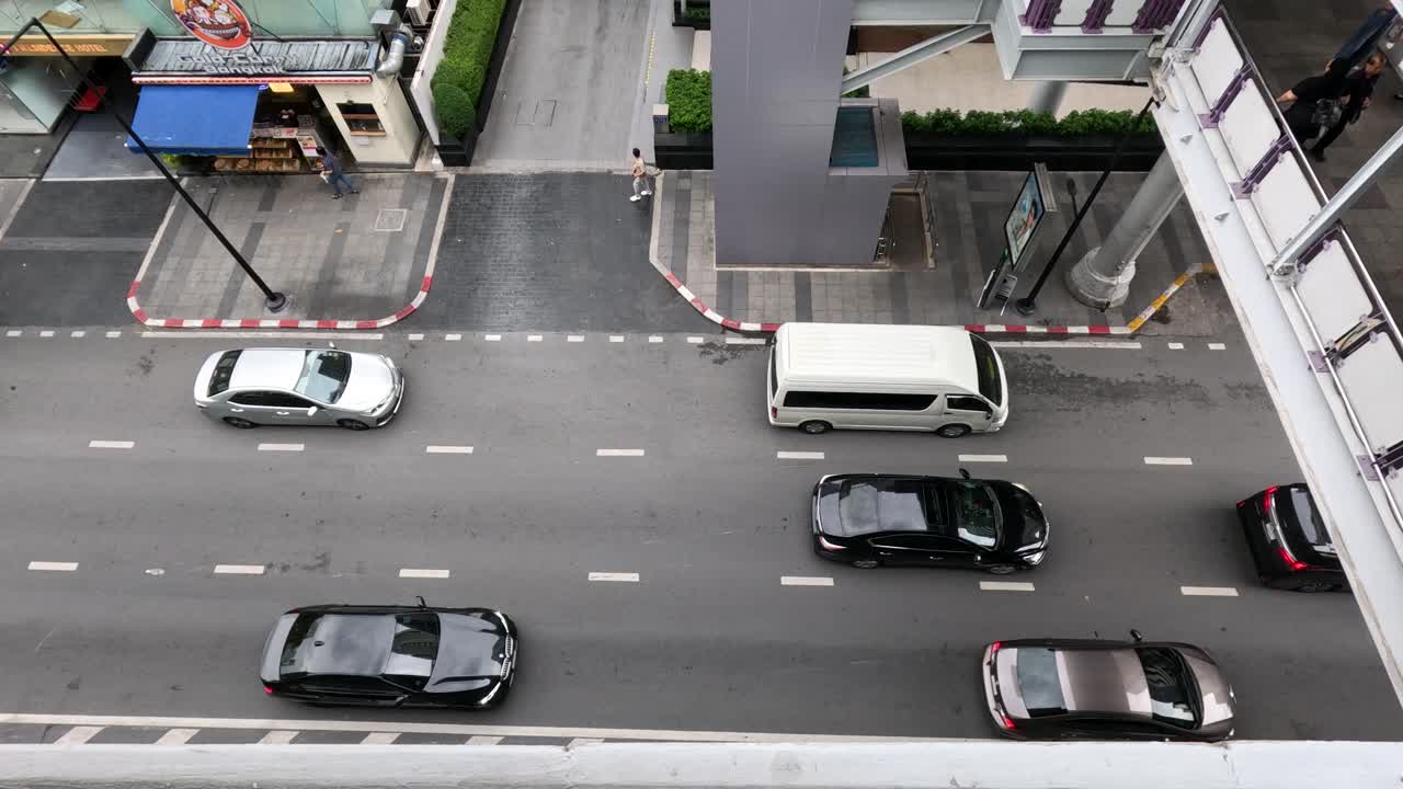 Overhead perspective of cars and vans driving on urban Bangkok street in daylight, steady camera